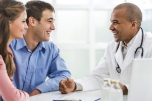 Cheerful African American doctor communicating with young couple in doctor's office.