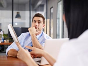 a caucasian male interviewer looking skeptical while listening to an asian female interviewee.