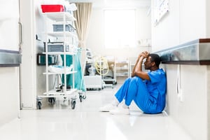 Sad male African American physician or nurse sitting in hallway_small-1