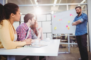 Male executive standing in front of colleagues during braintstorming in meeting room at creative office